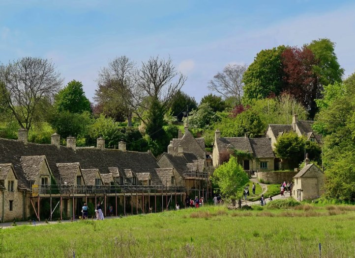 Honey-coloured Cotswold stone cottages above a water meadow, a stop on the combined day trips