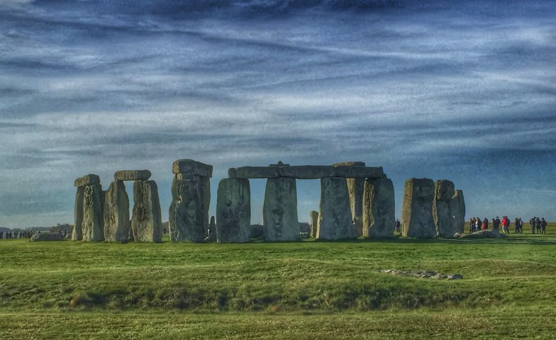 The Stonehenge sarsen circle on Salisbury Plain under a winter sky, with visitors on the path beyond the stones